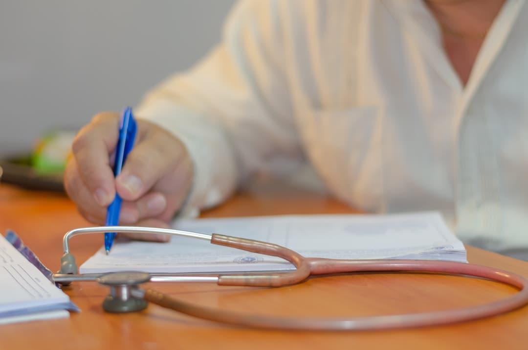 a person writing on a piece of paper with a stethoscope. Cover image for: AI-Assisted Referral Letter Generation From Clinical Encounters.