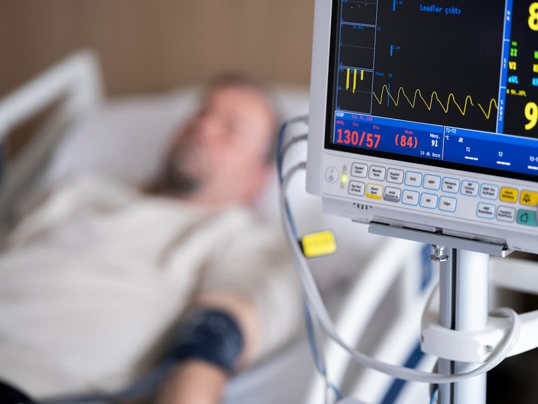 a man laying in a hospital bed next to a monitor. Cover image for: AI Medical Scribe for Emergency Medicine.