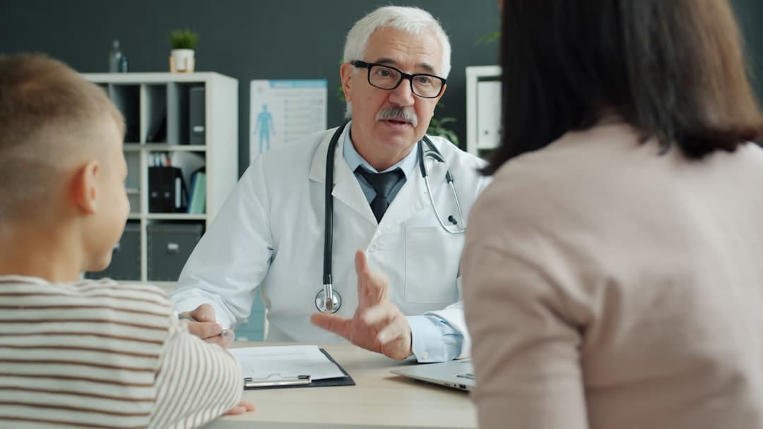 Doctor consults with mother and child in office.. Cover image for: AI Scribe for Ontario Family Medicine: PHIPA, OHIP Billing, and OSCAR EMR.
