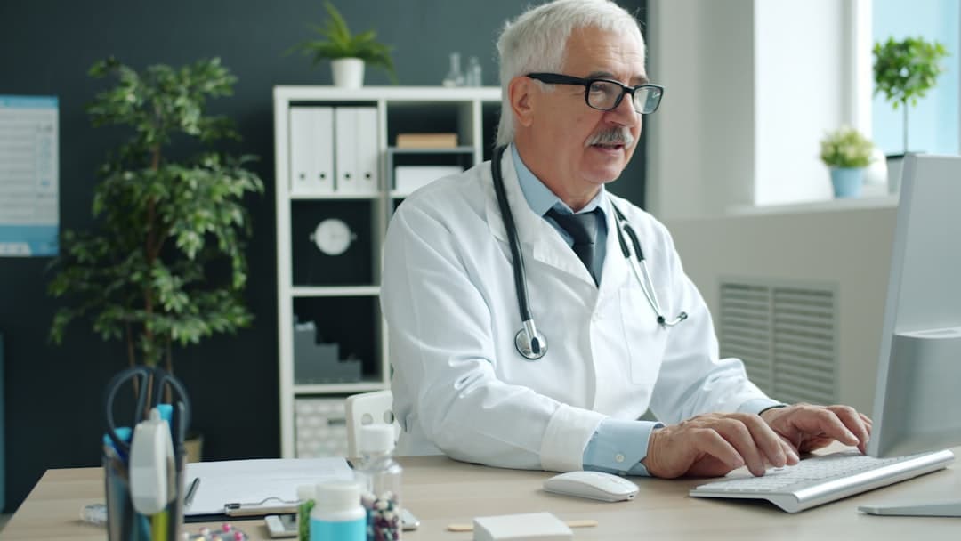 Doctor typing on computer in office. Cover image for: How AI Medical Scribes Reduce Physician Burnout.