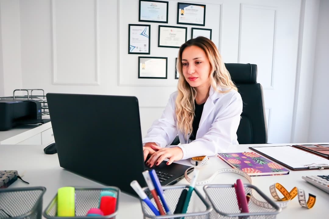 a woman sitting at a desk working on a laptop. Cover image for: Does Your AI Scribe Get Better Over Time? What Actually Improves.