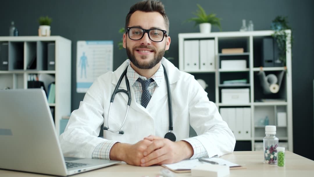 Doctor wearing a stethoscope sits at a desk.. Cover image for: AI Scribe for Patient Intake and History Documentation.