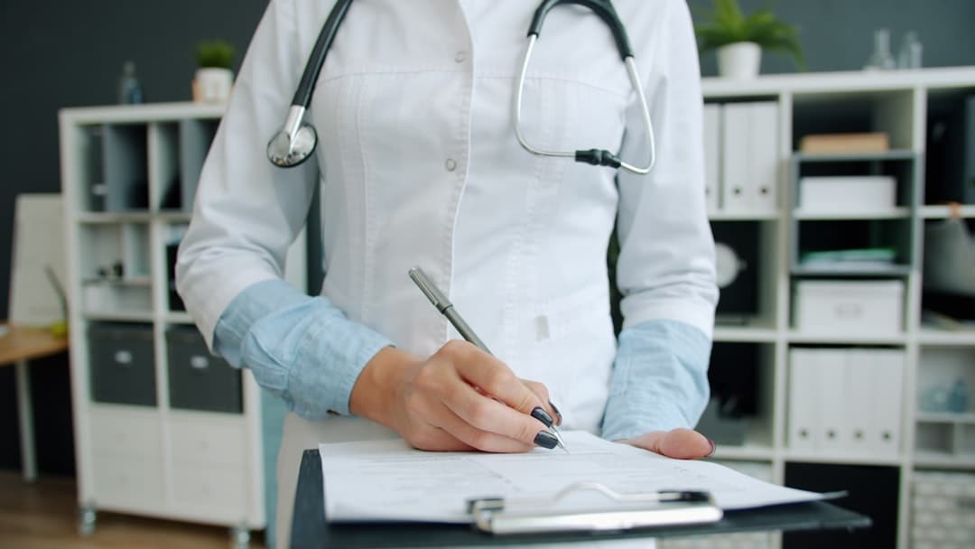 Doctor writing on clipboard in office. Cover image for: AI Scribe and the Patient Portal: Sharing the Note With Patients.