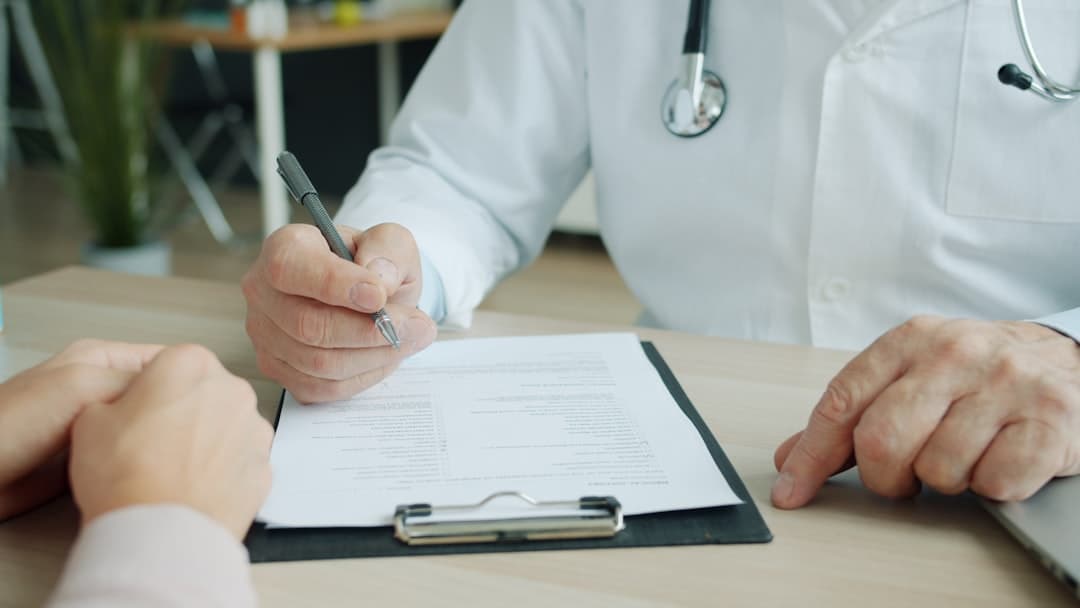 Doctor writing on a patient's chart. Cover image for: You Signed an AI-Generated Note With an Error: The Recovery Playbook.