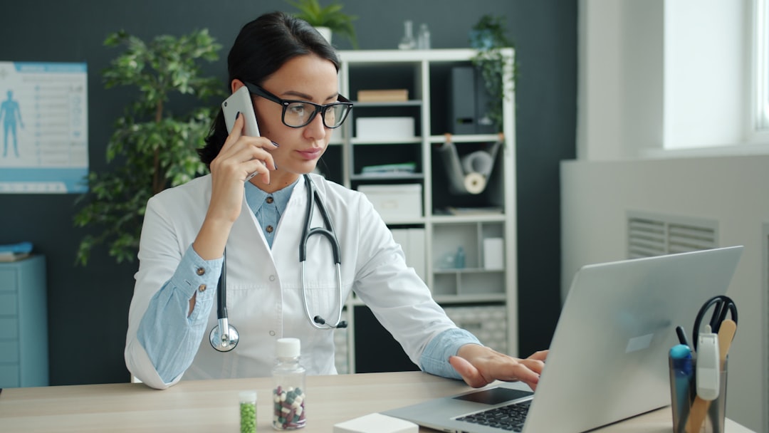Doctor on phone, working on laptop in office.. Cover image for: Six Months In: What to Re-evaluate About Your AI Scribe Setup.